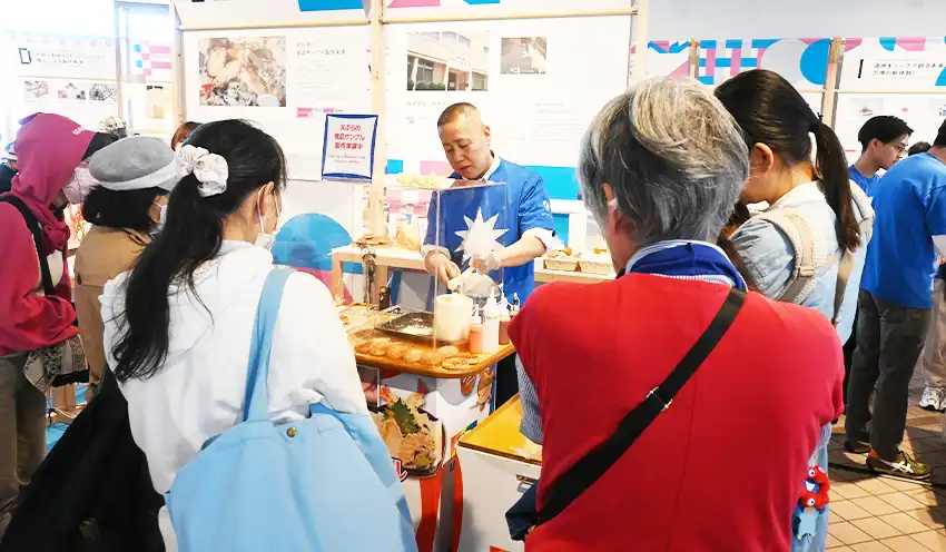 来場者に天ぷらの食品サンプルの製作を実演するいわさきの社員(中央奥、5月7日、大阪・関西万博会場)